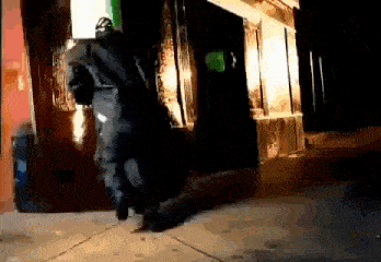 a man in a black suit is walking down the sidewalk in front of a building .