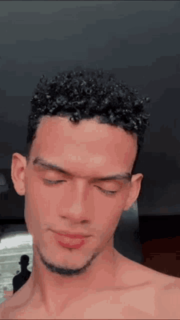 a man with curly hair and a beard is taking a selfie with his eyes closed .