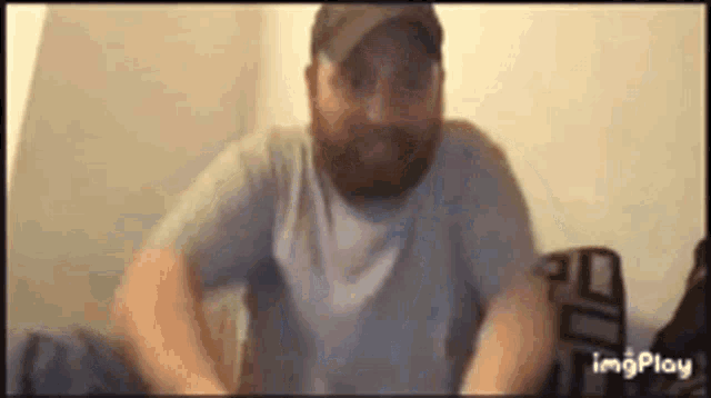 a man with a beard is sitting on a bed wearing a hat .