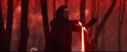 a man is holding a red lightsaber in the woods .