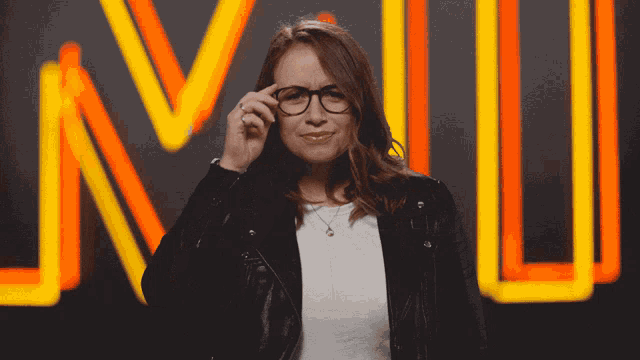 a woman adjusts her glasses in front of a neon sign that says nlu