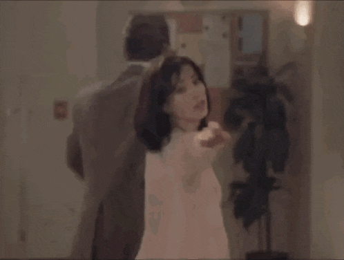 a man and a woman are dancing in a hallway in front of a plant .