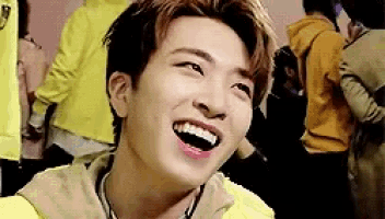 a young man wearing a yellow jacket is laughing with his mouth open .
