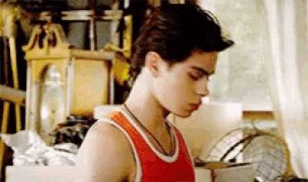 a young man wearing an orange tank top is standing in a room