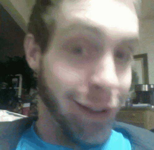a close up of a man 's face with a beard wearing a blue shirt