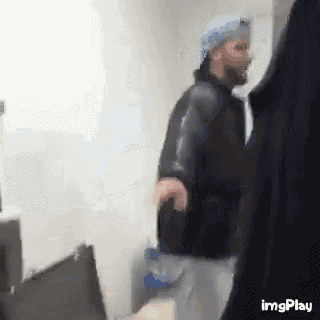 a man in a hat is standing in a room with a bottle of water .