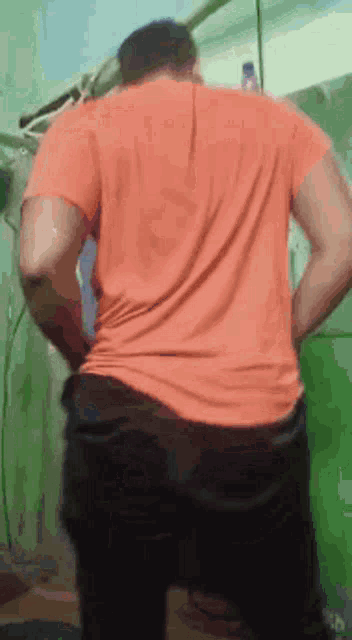 a man in an orange shirt is standing in a room with his hands on his hips