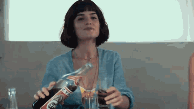 a woman is sitting at a table holding a bottle of coca cola and a glass .