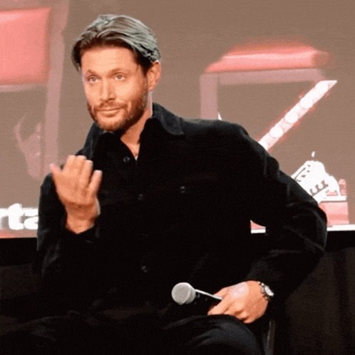 a man in a black shirt is holding a microphone and making a face