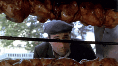a man in a hat is looking through a window at a bunch of meat