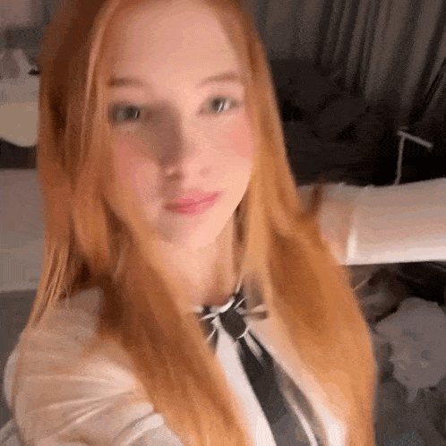 a young woman with long red hair is taking a selfie in a room with her arms outstretched .