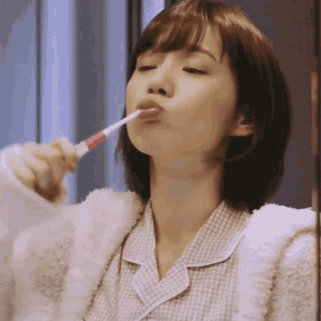 a woman is brushing her teeth with a red toothbrush