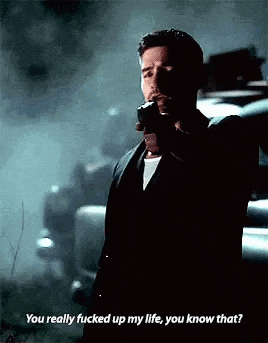 a man in a suit is holding a gun in his hand and talking to someone .