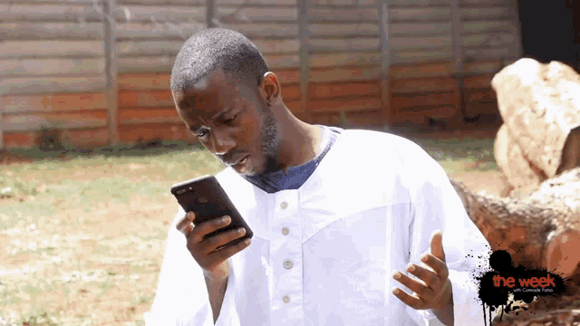 a man in a white shirt is looking at a cell phone with the week written on the bottom right