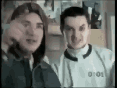 two men are standing next to each other and one of them is wearing a white shirt that says 0:01
