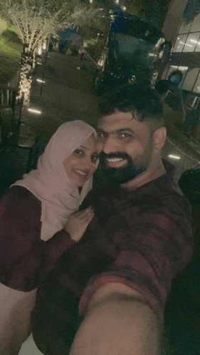 a man and woman are posing for a picture and the woman is wearing a pink hijab