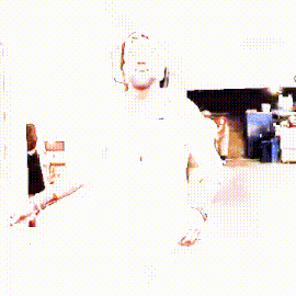 a man with a beard wearing a white shirt and a baseball cap is dancing in a hallway .