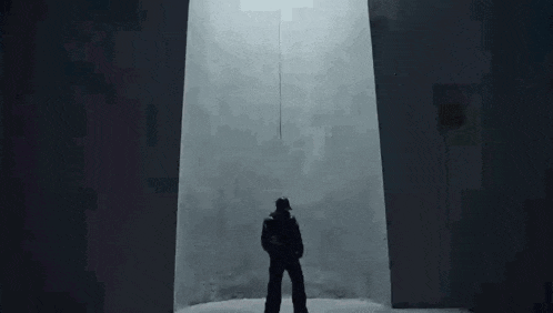 a man in a black jacket is standing in a dark room with a rope hanging from the ceiling .