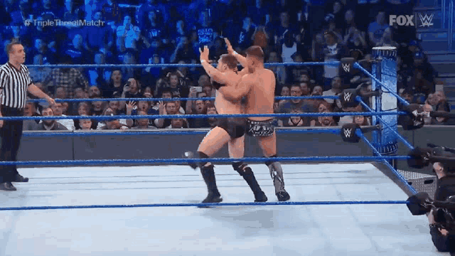 two men are wrestling in a ring with a referee watching .