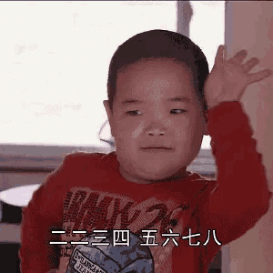 a young boy in a red shirt is waving his hand in a foreign language .