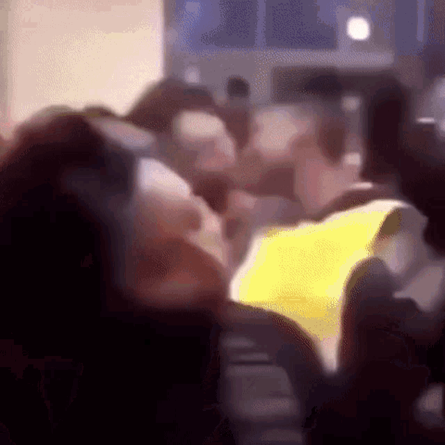 a group of people are sitting in a room and a man is wearing a yellow vest .