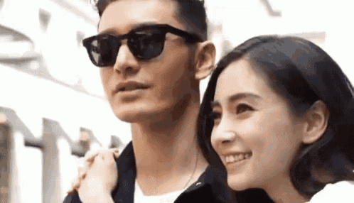a man and a woman are standing next to each other and smiling . the man is wearing sunglasses .