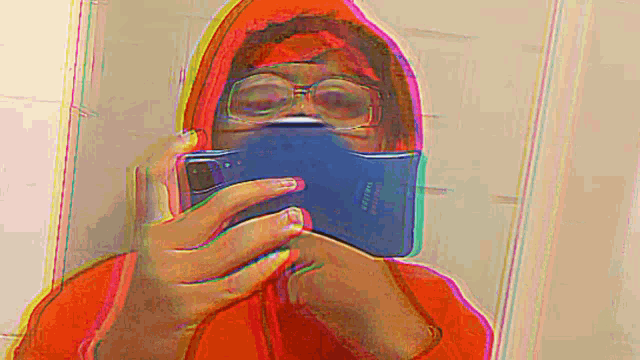 a person wearing a red hoodie and glasses is taking a selfie with their cell phone .