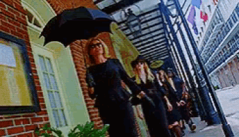 a woman in a black dress is holding an umbrella while walking down the street .
