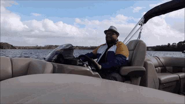 a man in a hat is driving a pontoon boat on a lake