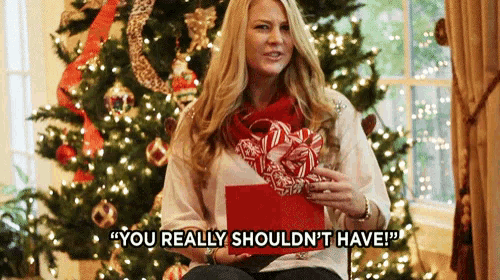 a woman is sitting in front of a christmas tree holding a gift and saying you really shouldn 't have