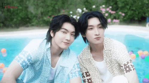 two young men are sitting next to each other in front of a pool .