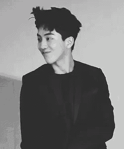 a black and white photo of a young man in a suit standing next to a wall .