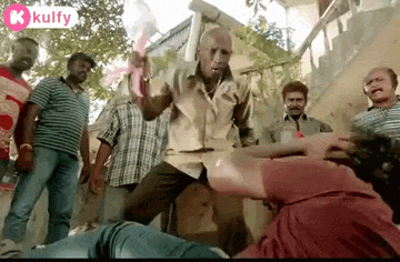 a group of men are standing around a man laying on the ground holding a bag .
