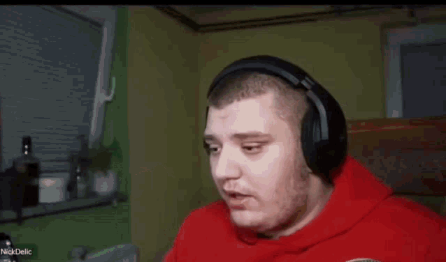 a man wearing headphones and a red hoodie is standing in a room with his hands in the air .