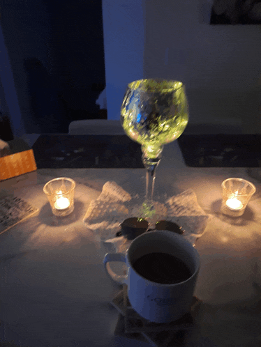 a cup of coffee sits on a table next to candles and a glass