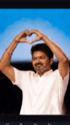 a man in a white shirt makes a heart shape with his hands
