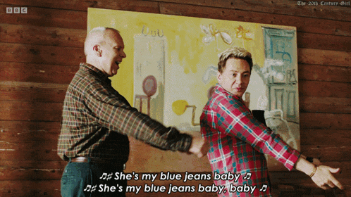 two men are dancing in front of a painting that says she 's my blue jeans baby on it
