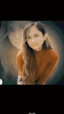 a girl in an orange sweater is standing in front of a blurred background