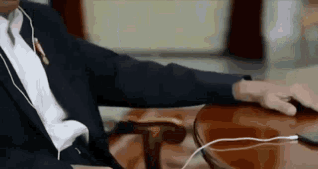 a man in a suit is sitting at a table with earbuds in his ears