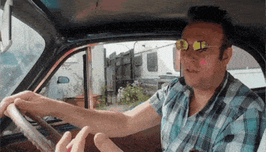 a man wearing sunglasses and a plaid shirt driving a car