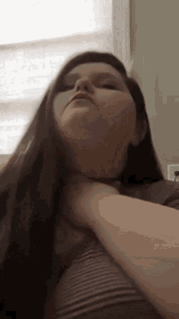 a woman is holding her neck with her hand while sitting in front of a window .