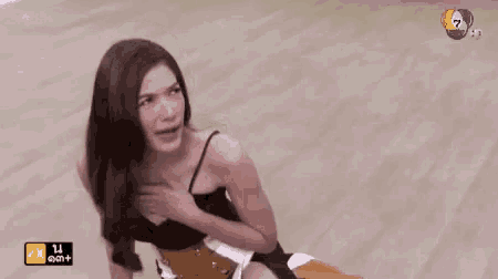 a woman is sitting on a wooden floor with her hand on her chest .