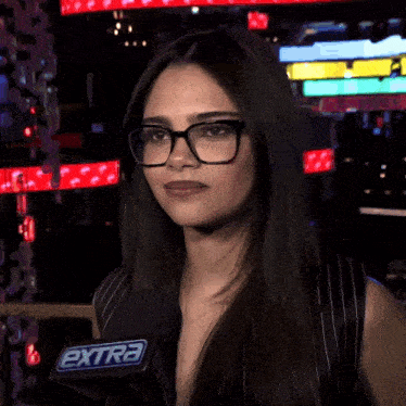 a woman wearing glasses and a microphone with the extra logo on it