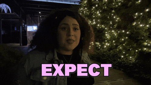 a woman stands in front of a sign that says expect shagarita