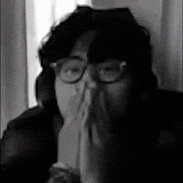 a black and white photo of a woman wearing glasses covering her mouth .