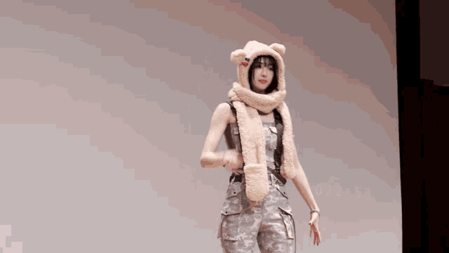a woman wearing a teddy bear hat and scarf stands in front of a projector screen