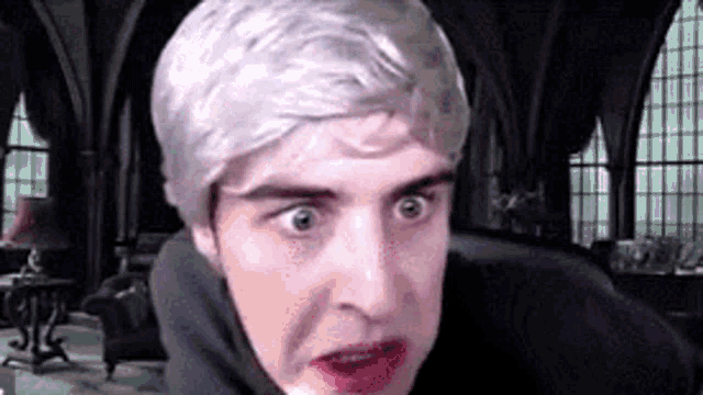 a man with white hair and red lips is making a funny face in a living room .
