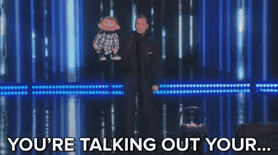 a man in a suit is holding a puppet and says you 're talking out your ..
