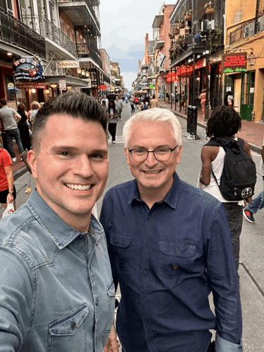 two men are posing for a picture in front of a building that has the word cigars on it