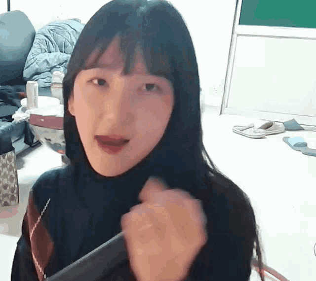 a girl with long black hair and bangs is holding a hair straightener in her hand .